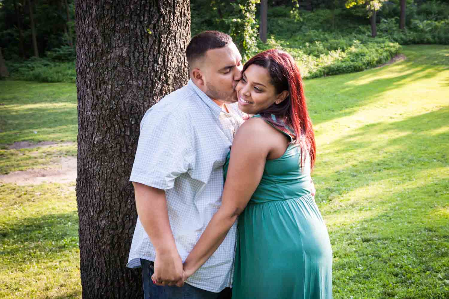 Man kissing woman on cheek beside tree during a Central Park engagement shoot