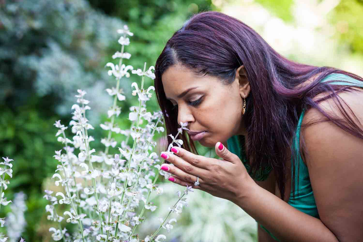 Woman wearing engagement ring leaning down and smelling flower