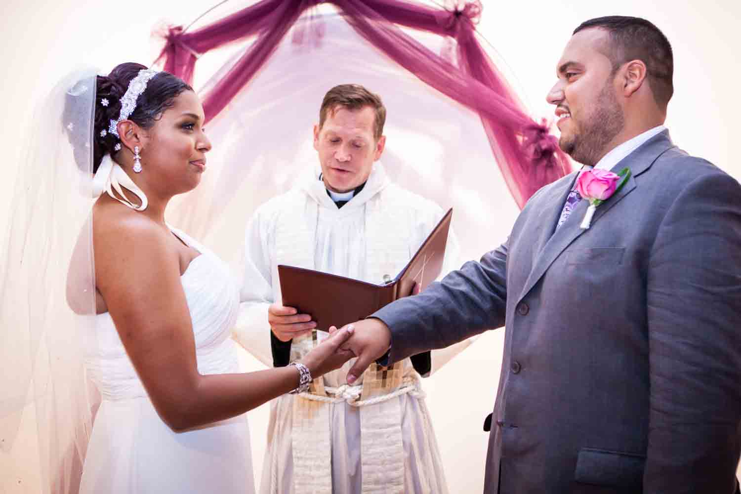 Bride and groom holding hands in front of priest at an Attic Studios wedding
