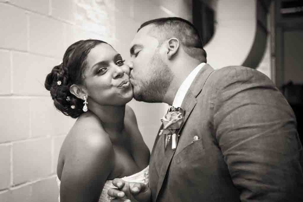 Black and white photo of groom kissing bride on cheek