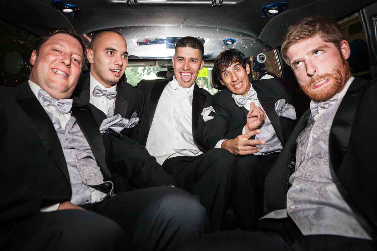 Groom and groomsmen making funny faces in the back of a limo