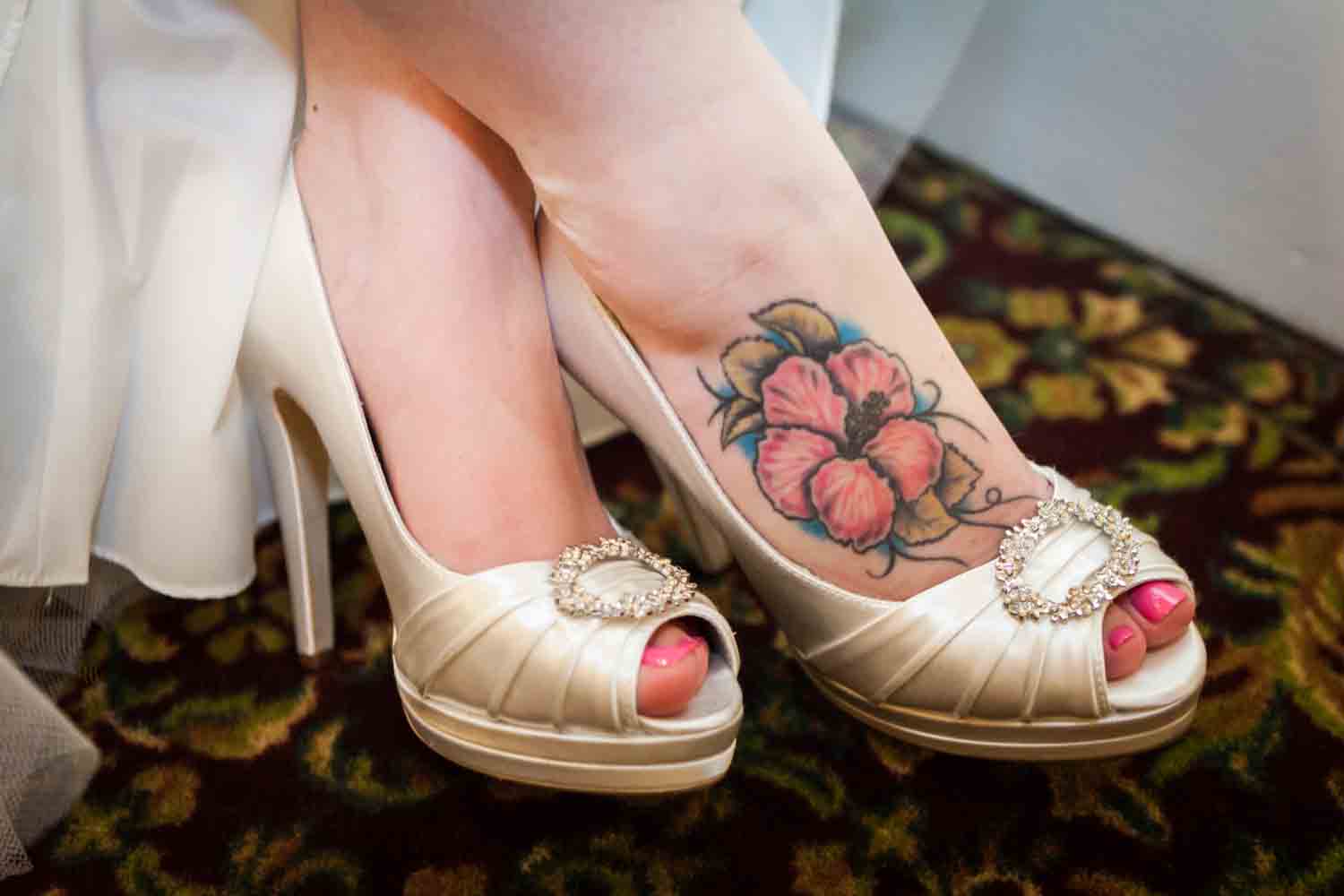 Close up on bride's feet with flower tattoo and satin high heels