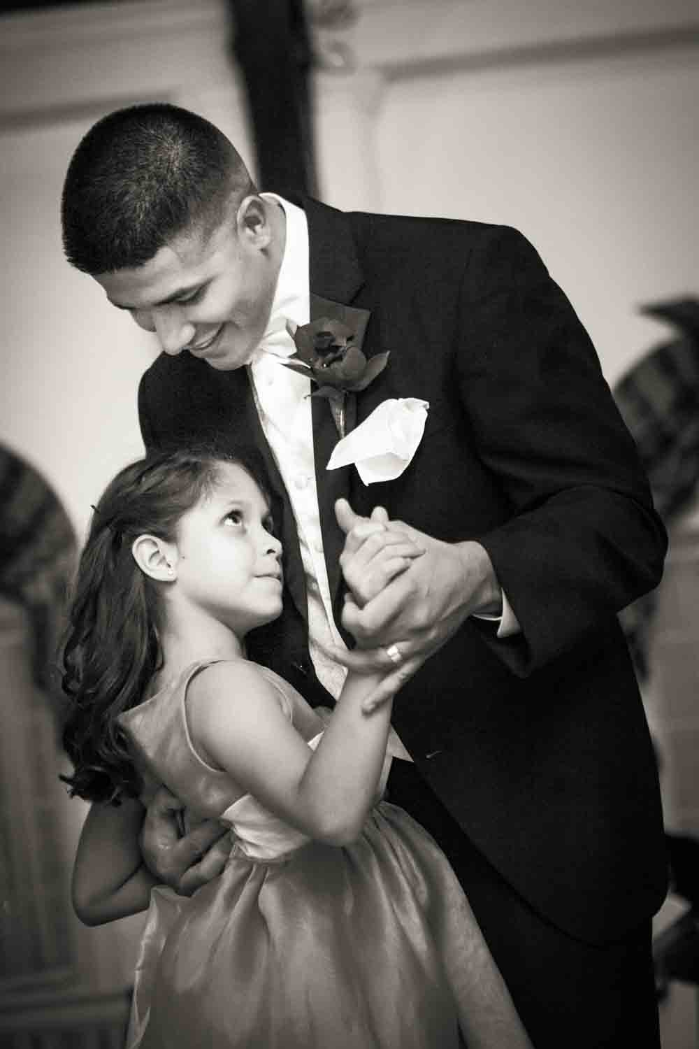 Black and white photo of groom dancing with little girl at a Fort Hamilton Community Center wedding