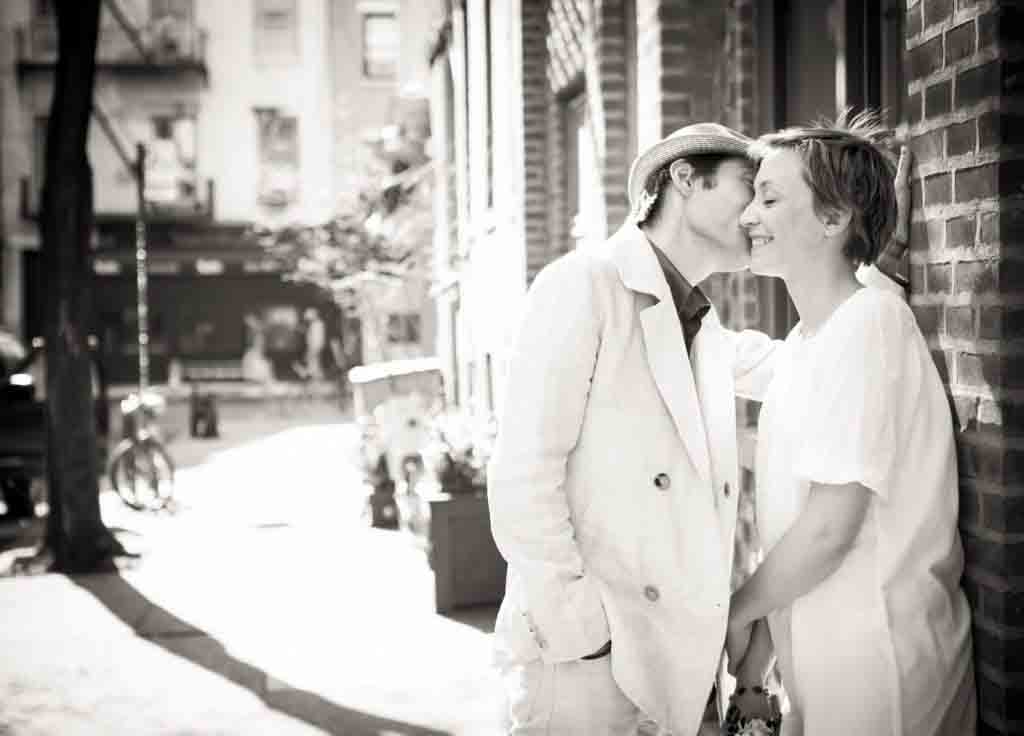 Black and white photo of man kissing woman against brick wall