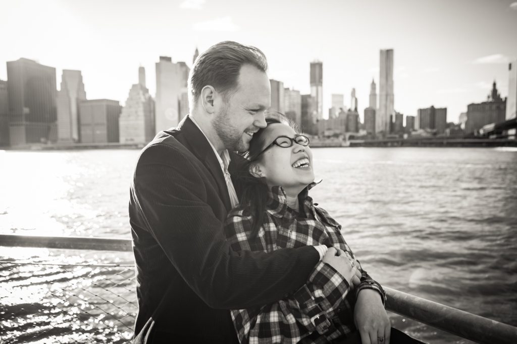 Black and white photo of couple in front of East River with NYC skyline in background