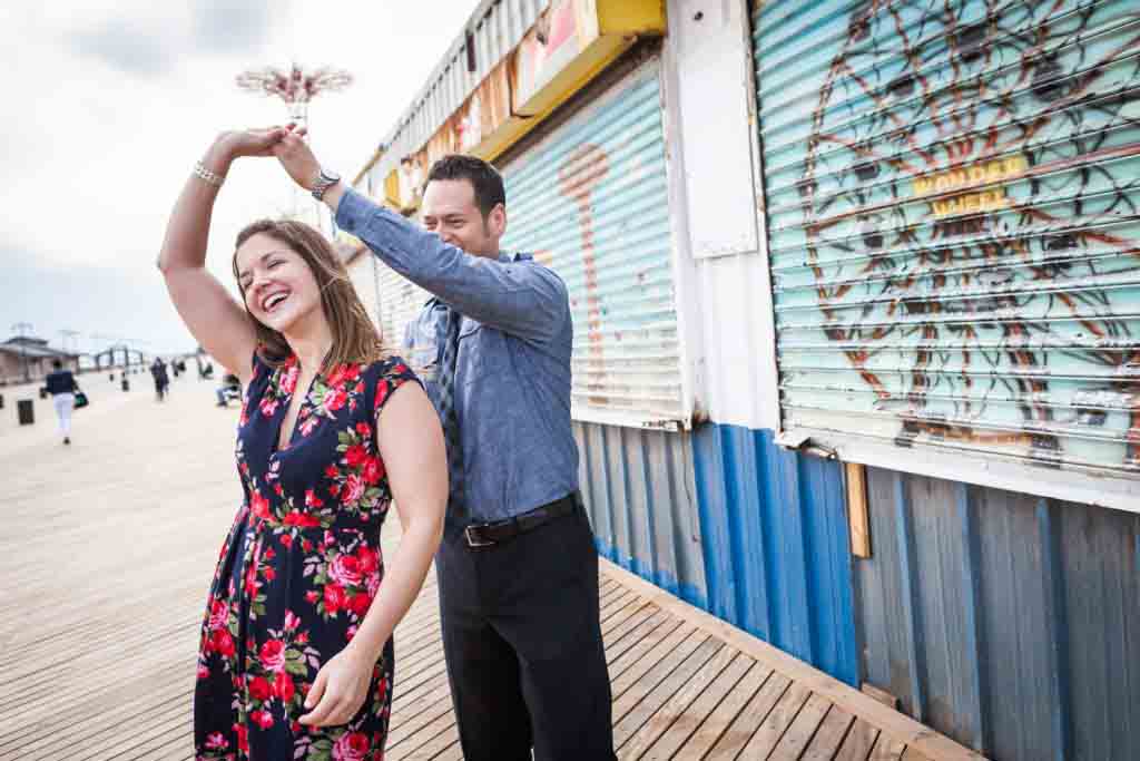 Couple dancing on boardwalk in front of mirror Couple sitting on rock by beach for an article on Coney Island engagement photo tips