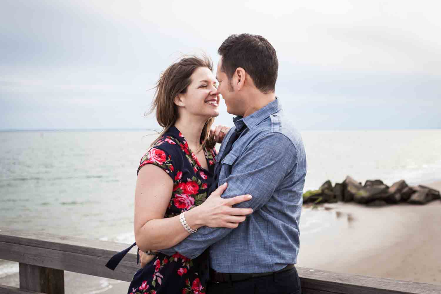 Couple together against pier railing Couple dancing on boardwalk in front of mirror Couple sitting on rock by beach for an article on Coney Island engagement photo tips