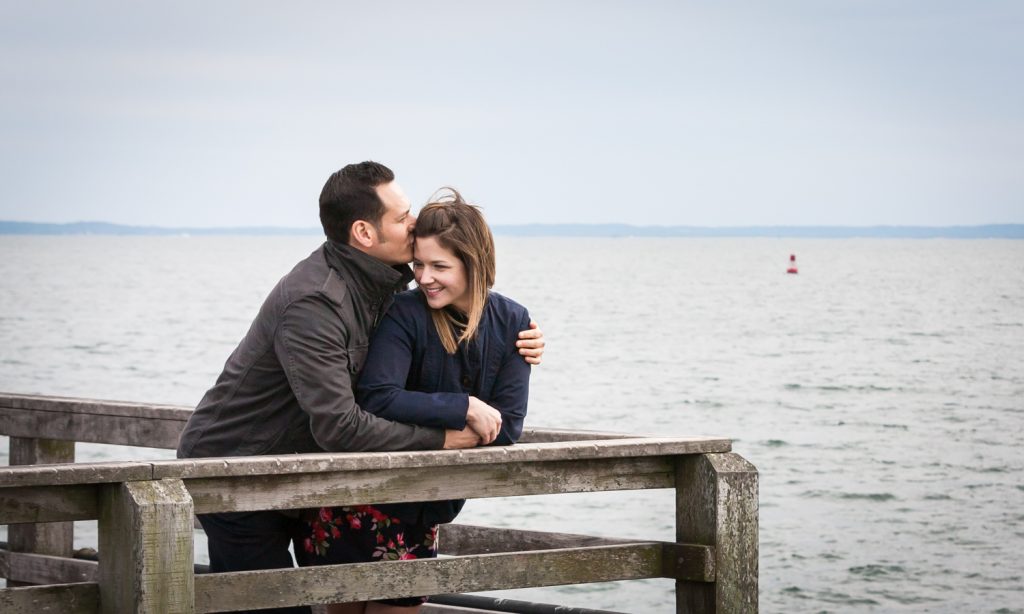 Man kissing woman against railing of pier for an article on Coney Island engagement photo tips