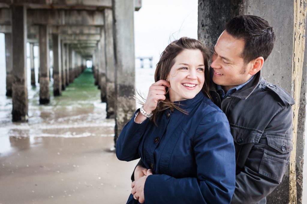Couple leaning against column under boardwalk for an article on Coney Island engagement photo tips