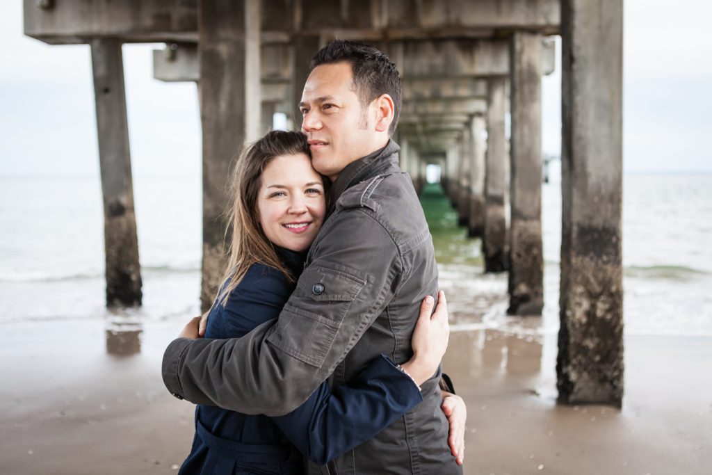 Couple hugging under boardwalk pier for an article on Coney Island engagement photo tips