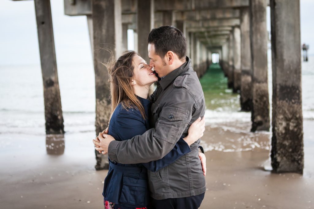 Couple kissing under boardwalk pier for an article on Coney Island engagement photo tips