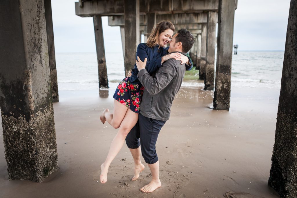 Man lifting up woman under boardwalk pier for an article on Coney Island engagement photo tips