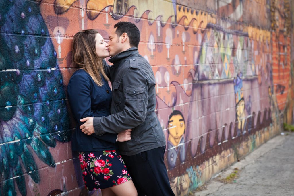 Couple kissing against colorful mural at Coney Island