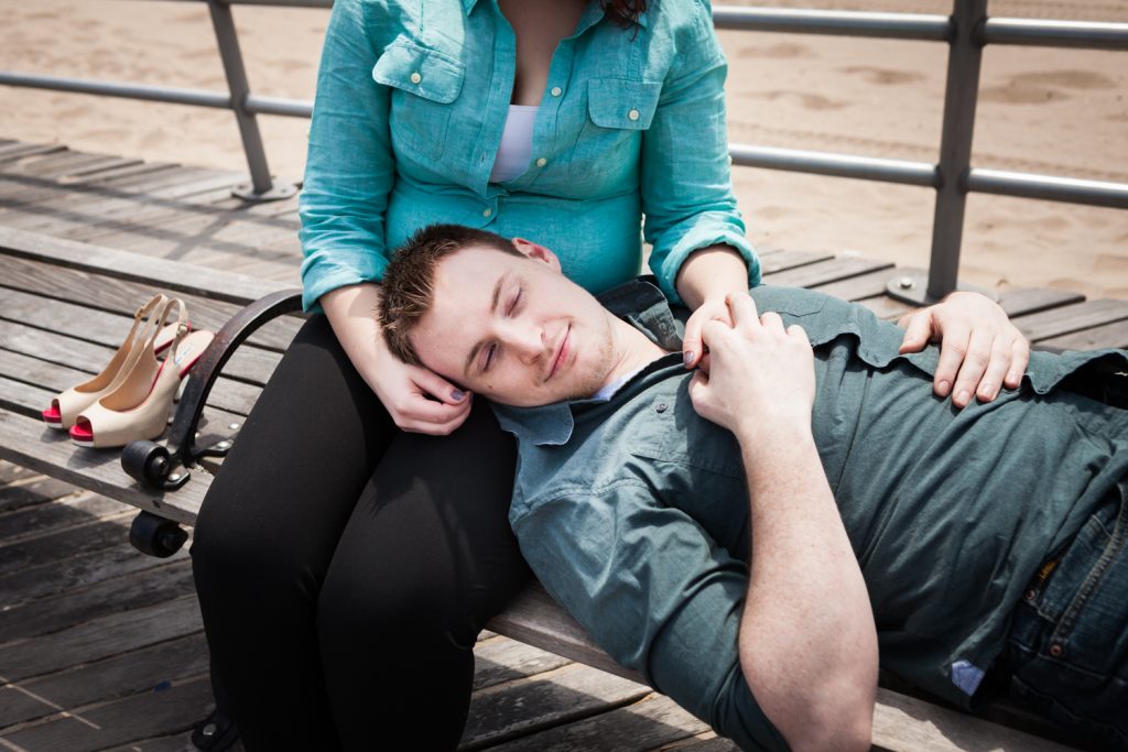 Coney Island engagement photos of man with head in woman's lap on bench