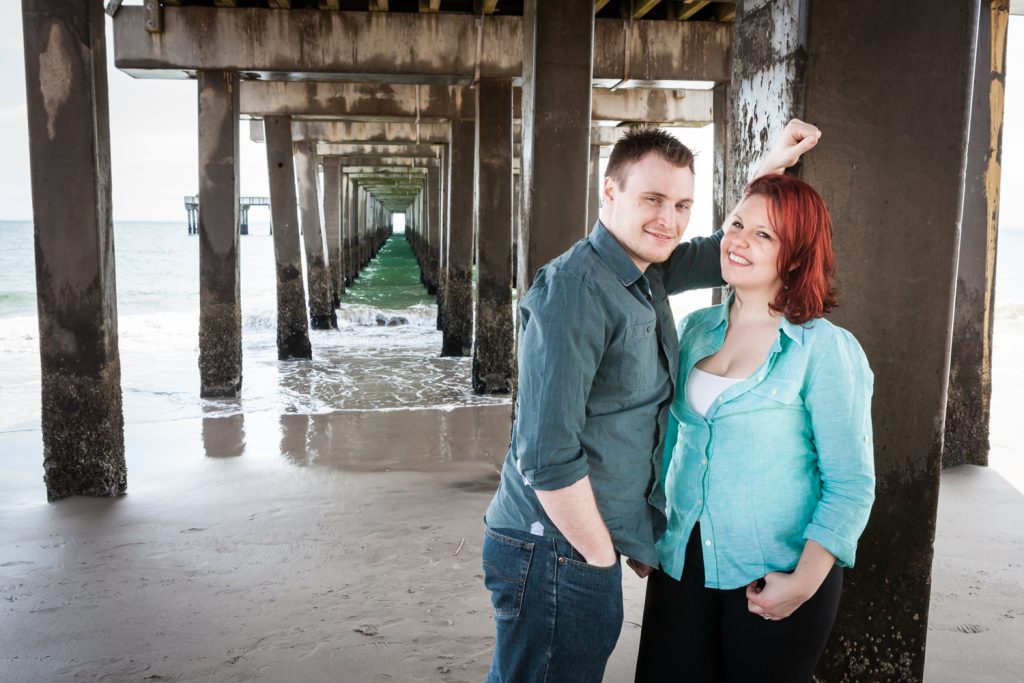 Coney Island engagement photos of couple leaning against column under pier