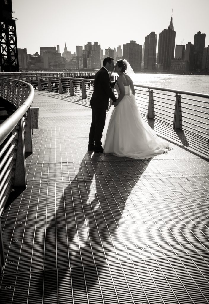 Bride and groom kissing with long shadow in Gantry Plaza State Park