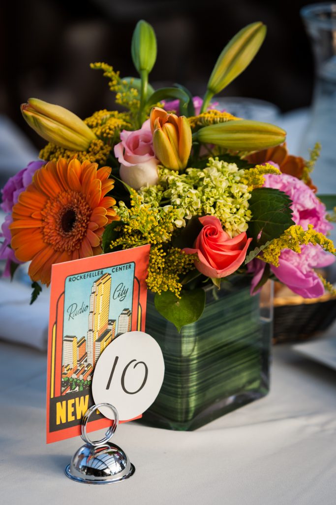 Flower centerpiece and table number with NYC postcard at a Ravel Hotel Penthouse wedding