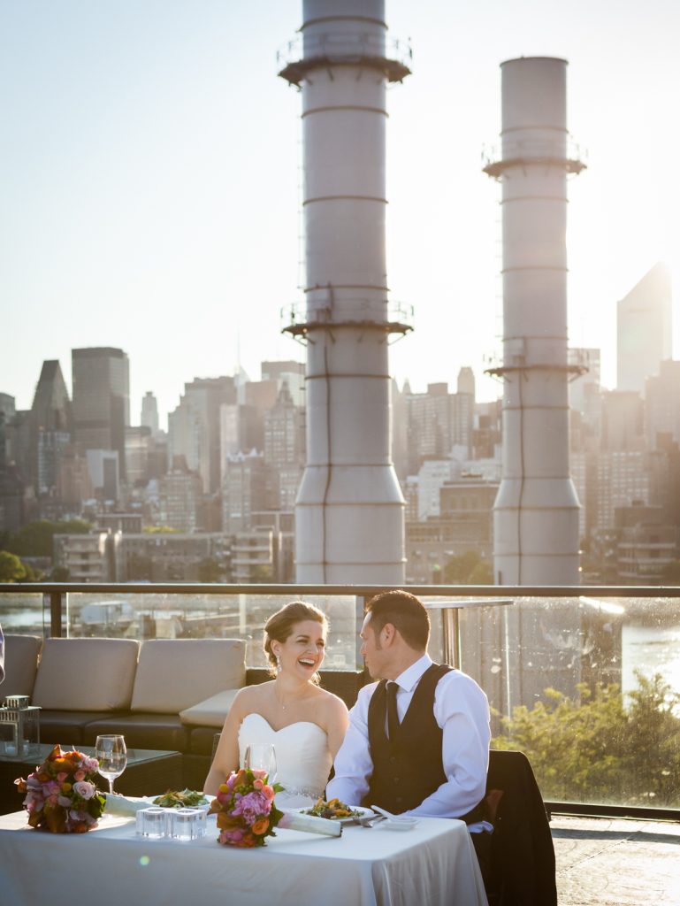 Bride and groom at sweetheart table with Long Island City smoke stacks in background at a Ravel Hotel Penthouse wedding