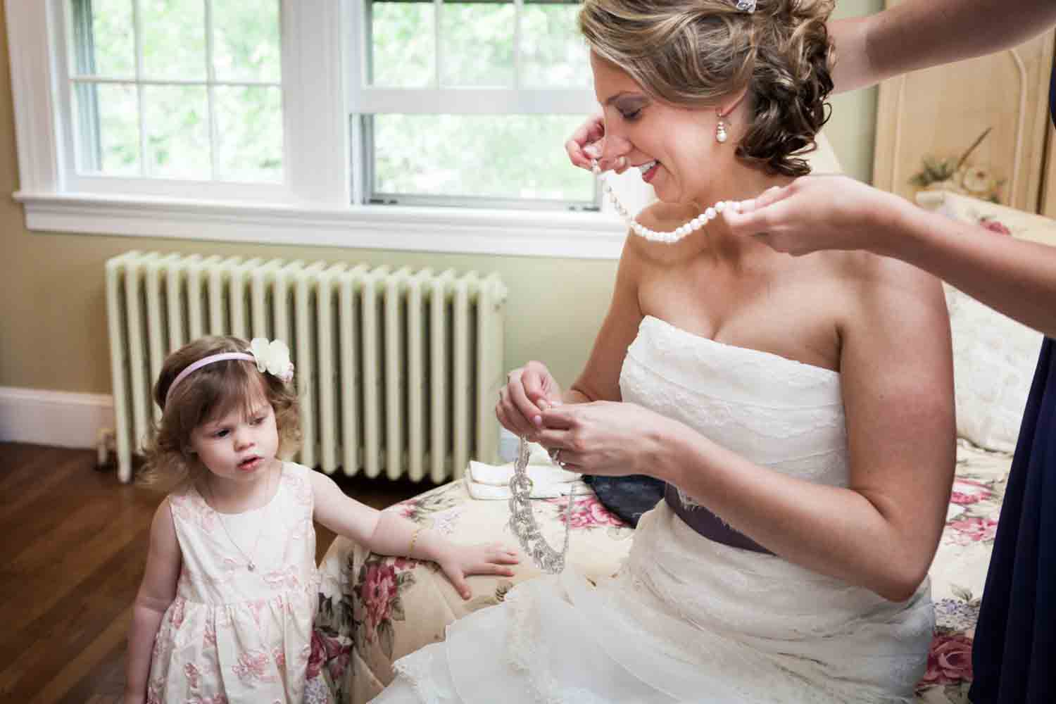 Little girl watching bride put on jewelry