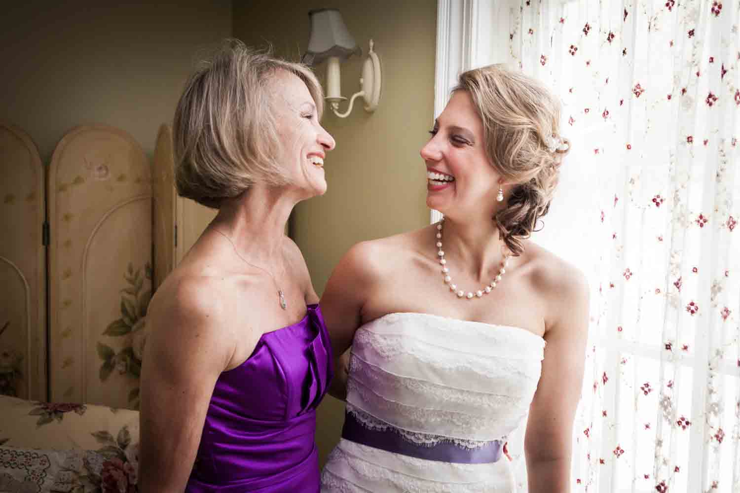 Bride and mother laughing by window