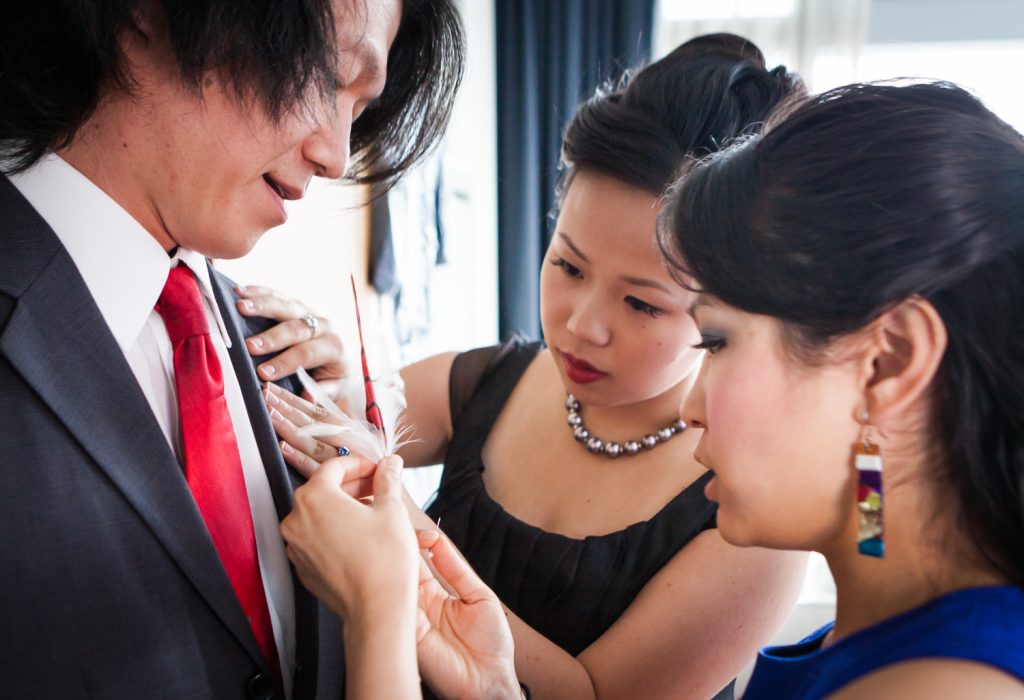 Two women putting feather boutonniere on groomsman