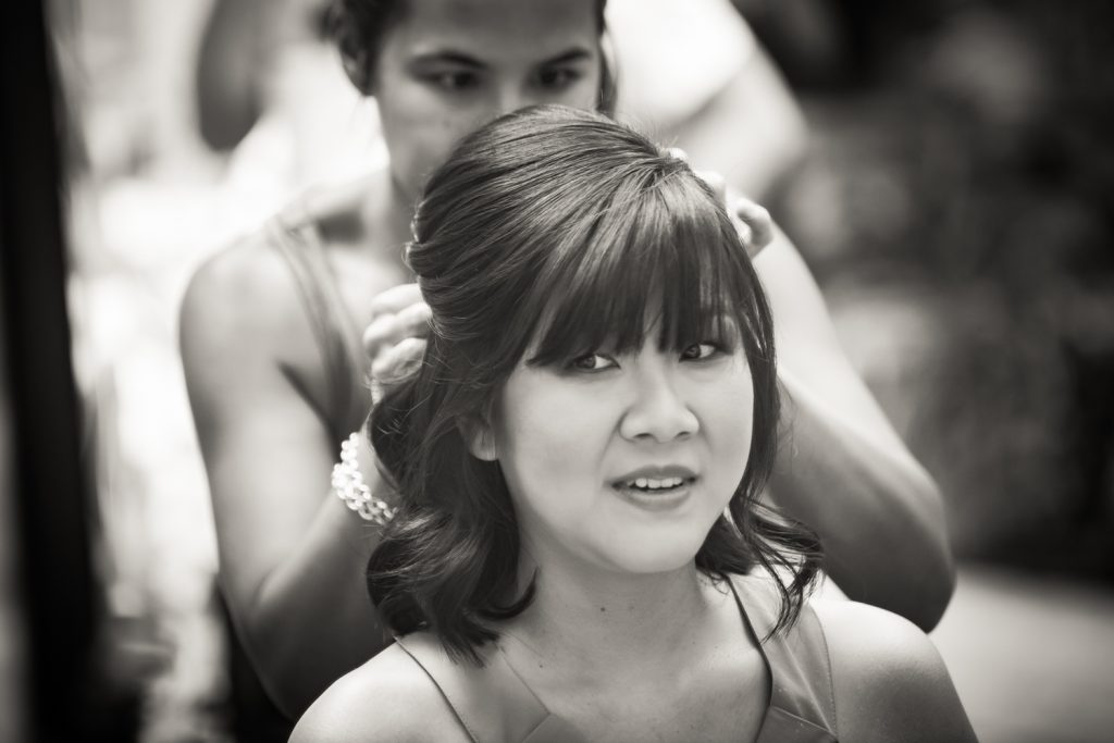 Black and white photo of bride looking in mirror while getting hair done