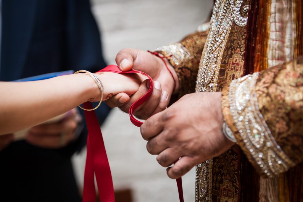 Close up on groom tying bride's hand with red ribbon during ceremony