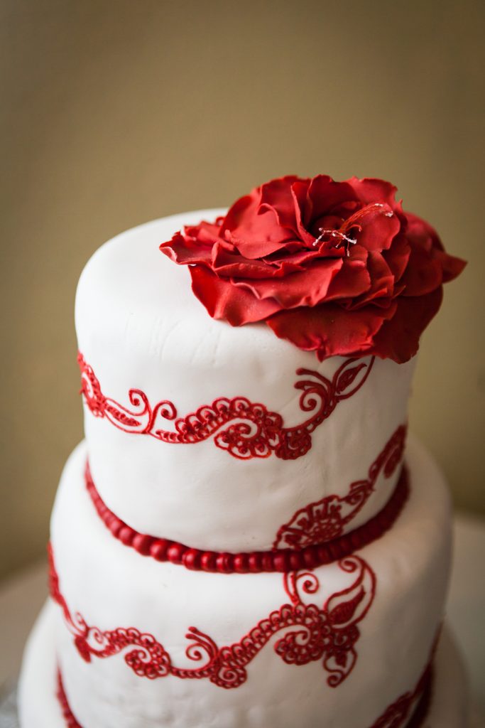 Wedding cake with red filigree icing and red flower on top