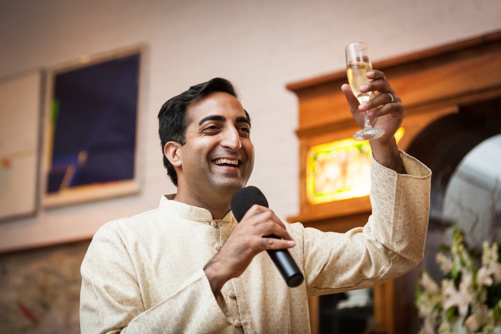 Best man wearing Indian attire holding up a champagne glass during speech