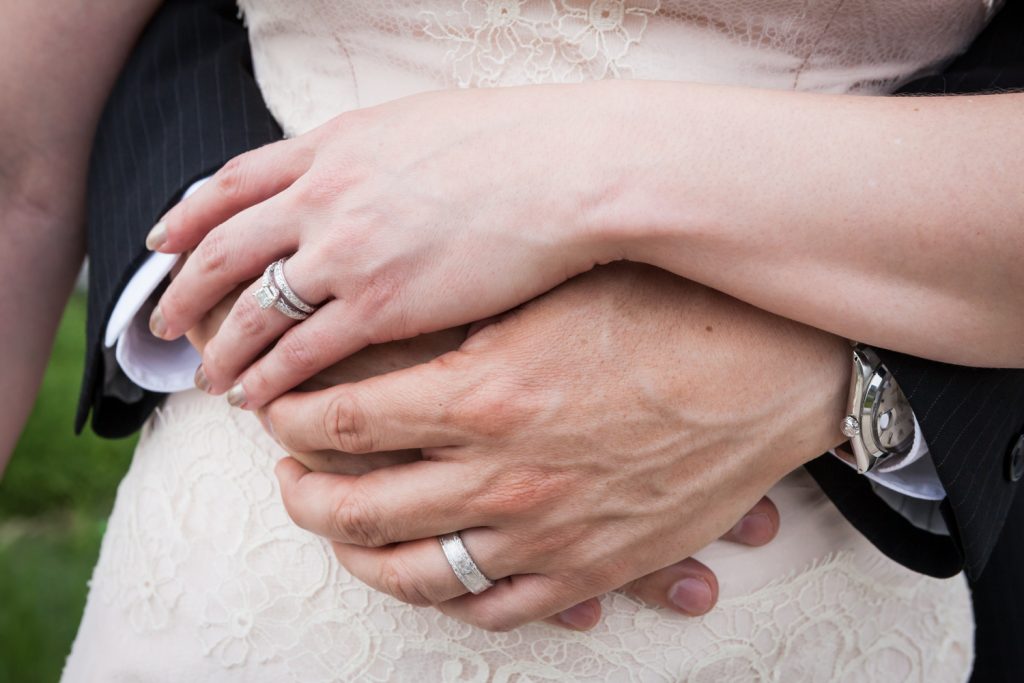 Close up on bride and groom clasping hands and wearing wedding rings