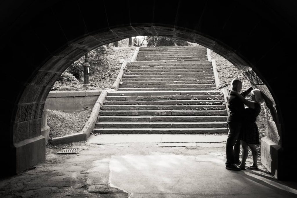 Black and white photo of couple leaning against side of Trefoil Arch in Central Park