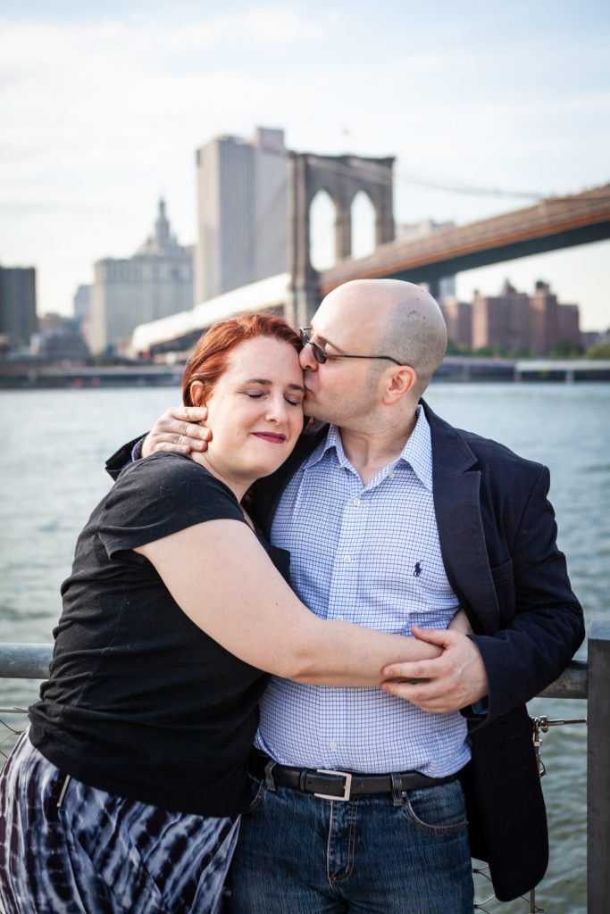 Man kissing woman on cheek with Brooklyn Bridge in background during a Brooklyn Bridge Park engagement portrait session