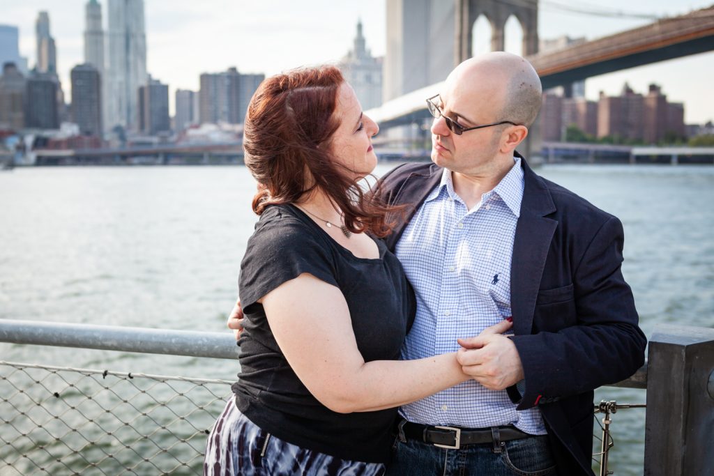 Couple hugging with Brooklyn Bridge in background during a Brooklyn Bridge Park engagement portrait session