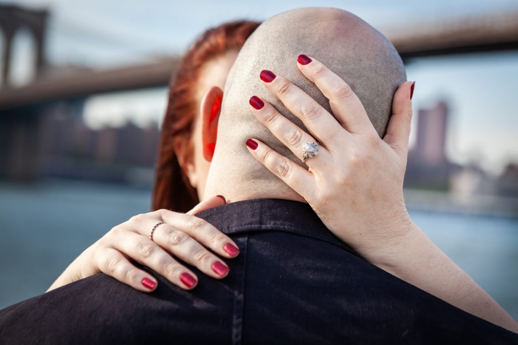 Close up of woman's hand wearing engagement ring on the back of man's bald head