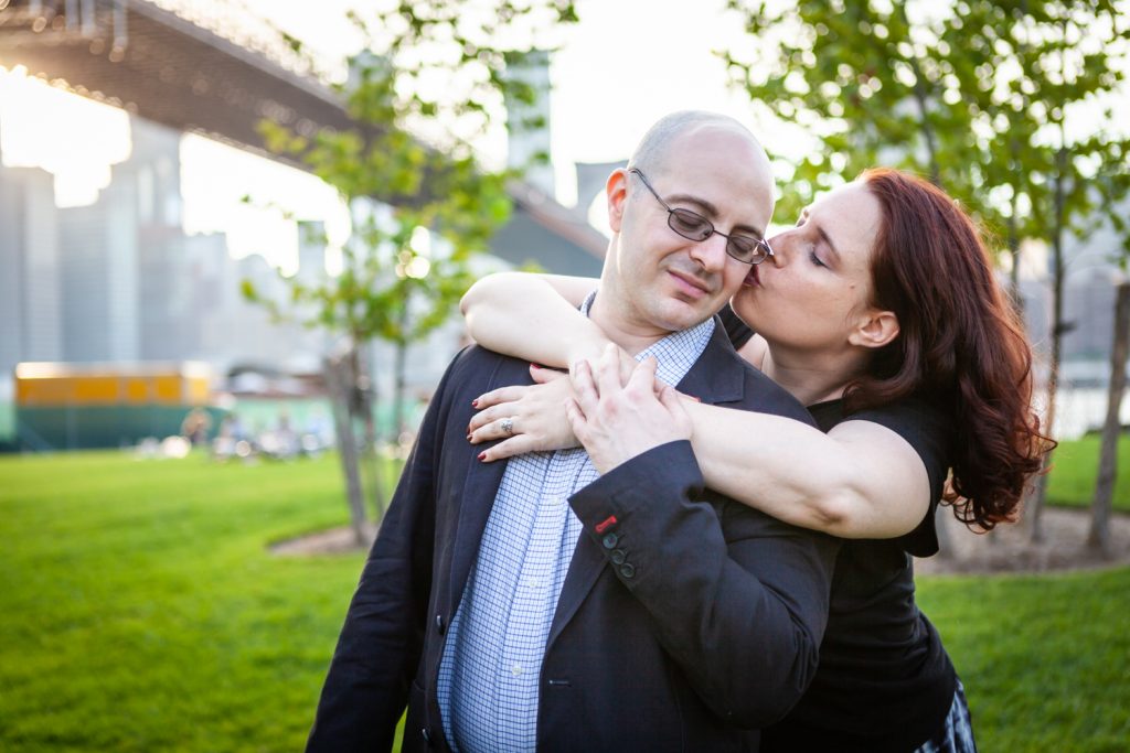Woman kissing man on cheek during a Brooklyn Bridge Park engagement portrait session
