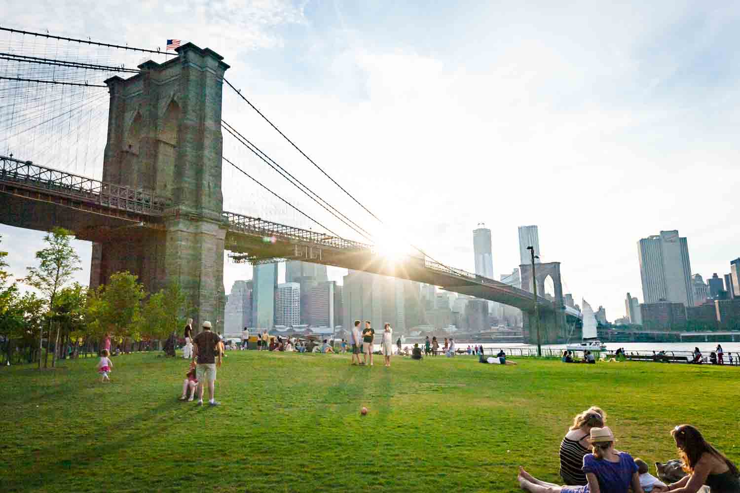 Wide view of Brooklyn Bridge Park with bridge and NYC skyline in view at sunset