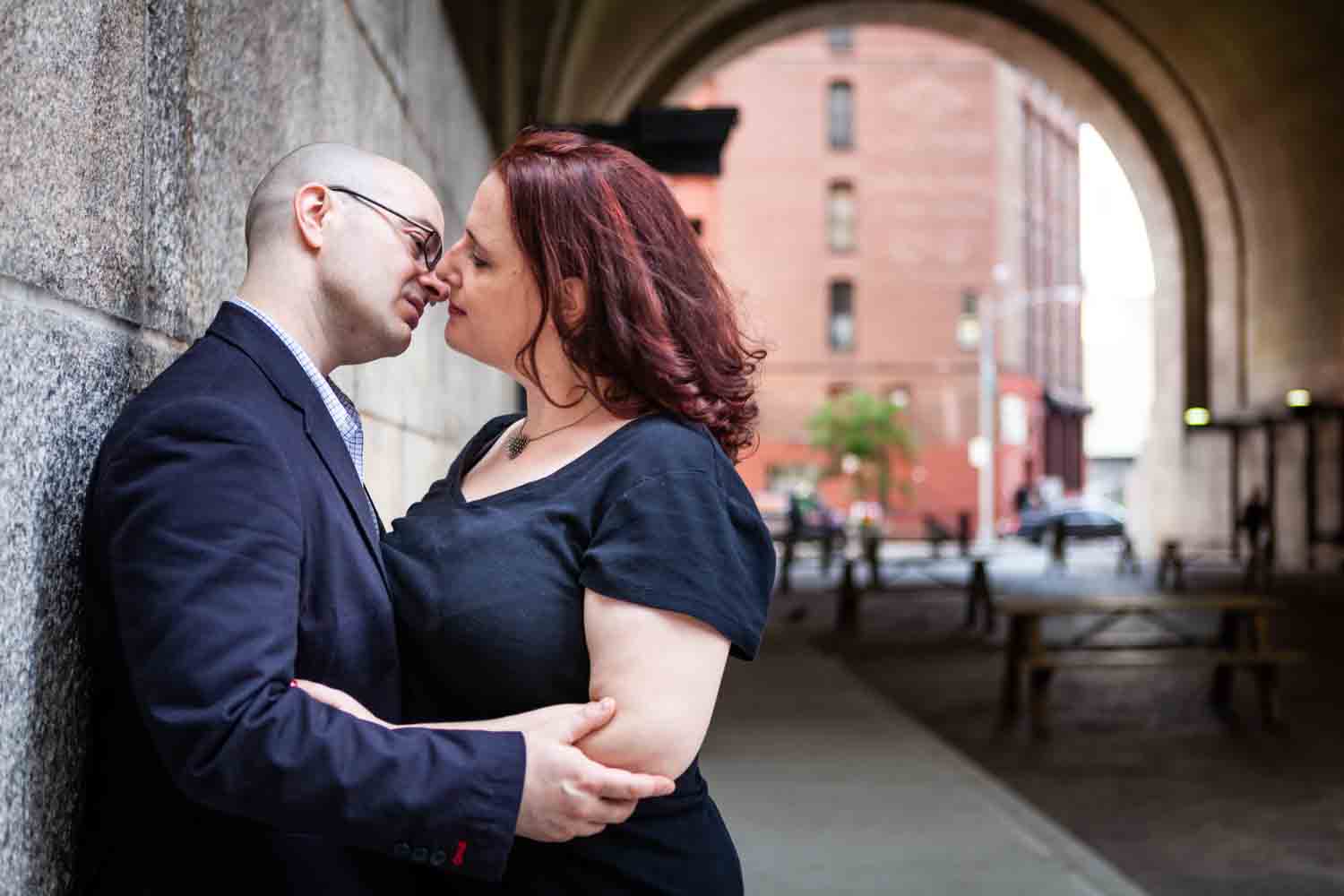 Couple about to kiss while leaning on wall of DUMBO Archway