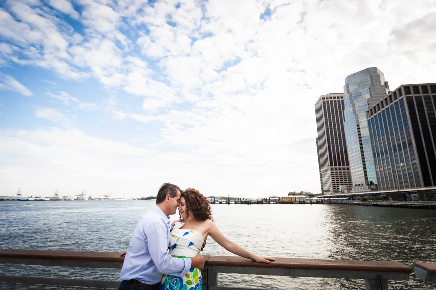 Financial District engagement photos of couple cuddling on railing in front of waterfront