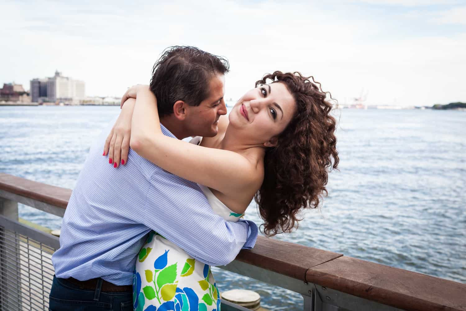 Financial District engagement photos of couple hugging by railing in front of waterfront