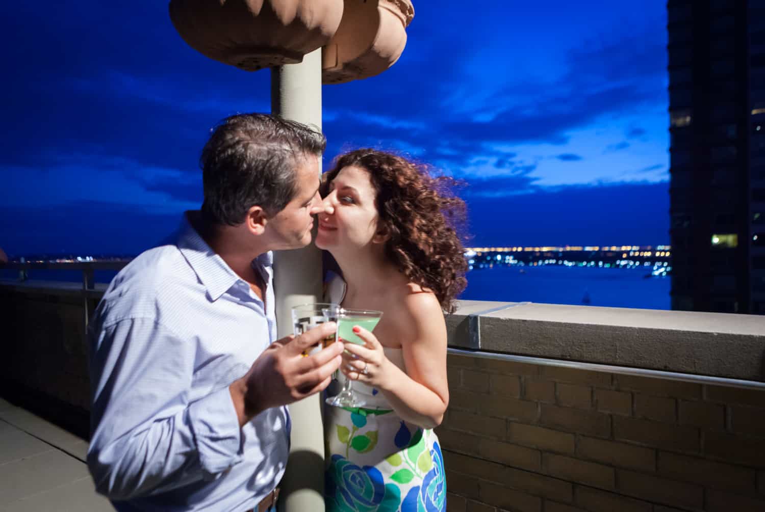 Couple kissing and holding cocktails on rooftop