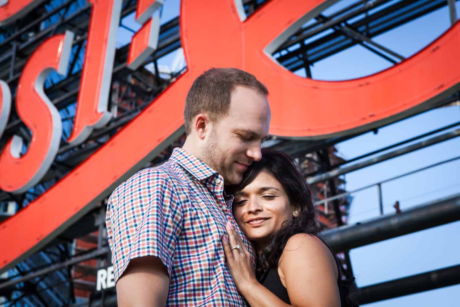 Couple hugging under Pepsi Cola neon sign at a Gantry Plaza State Park engagement shoot