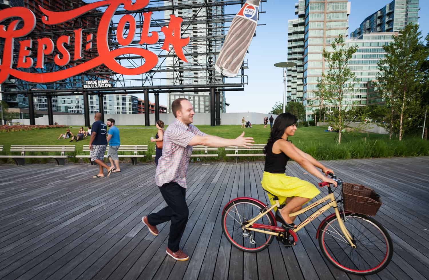 Man chasing woman on bicycle at a Gantry Plaza State Park engagement shoot