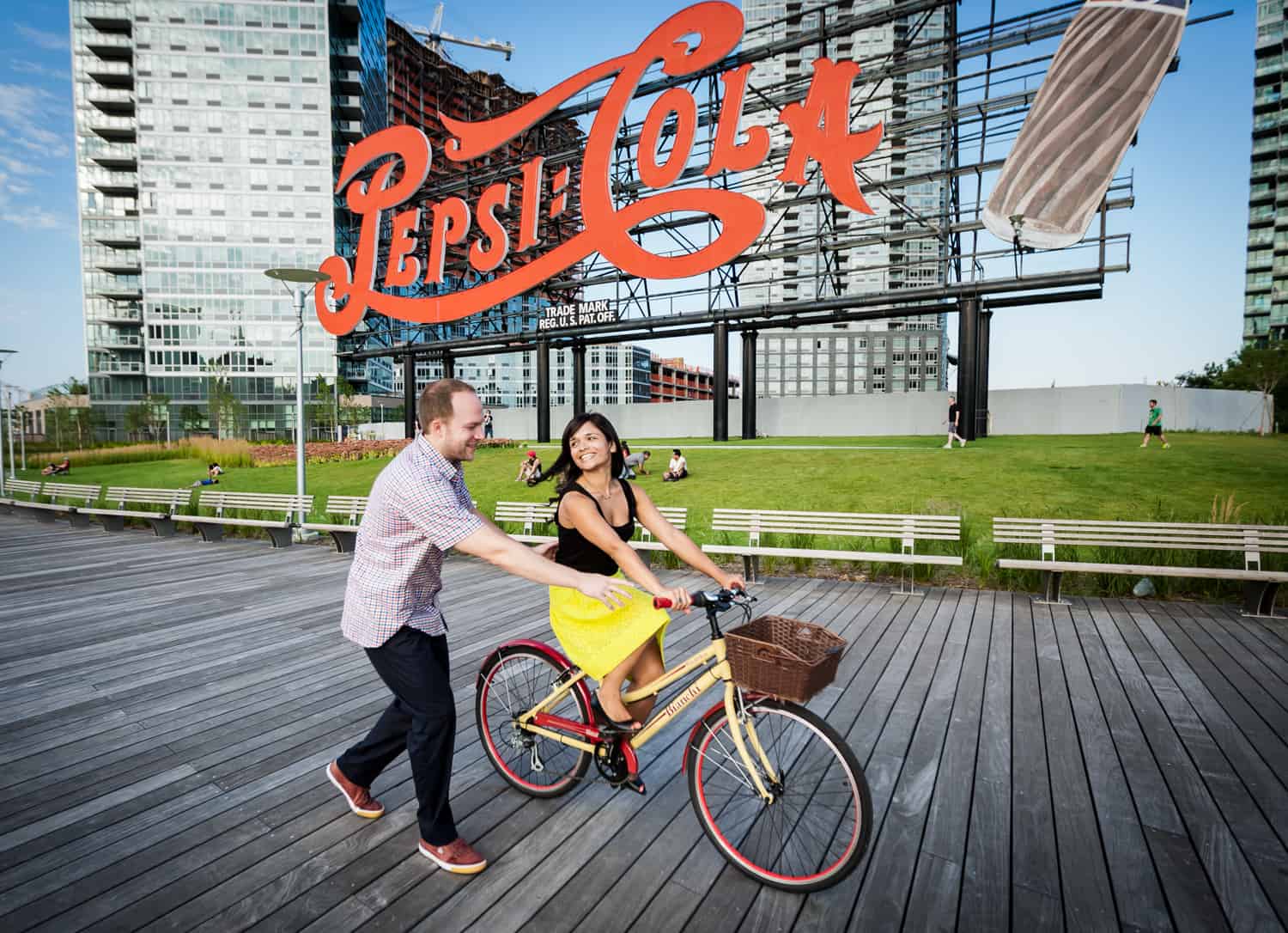 Man chasing woman on bike under Pepsi Cola sign at a Gantry Plaza State Park engagement shoot