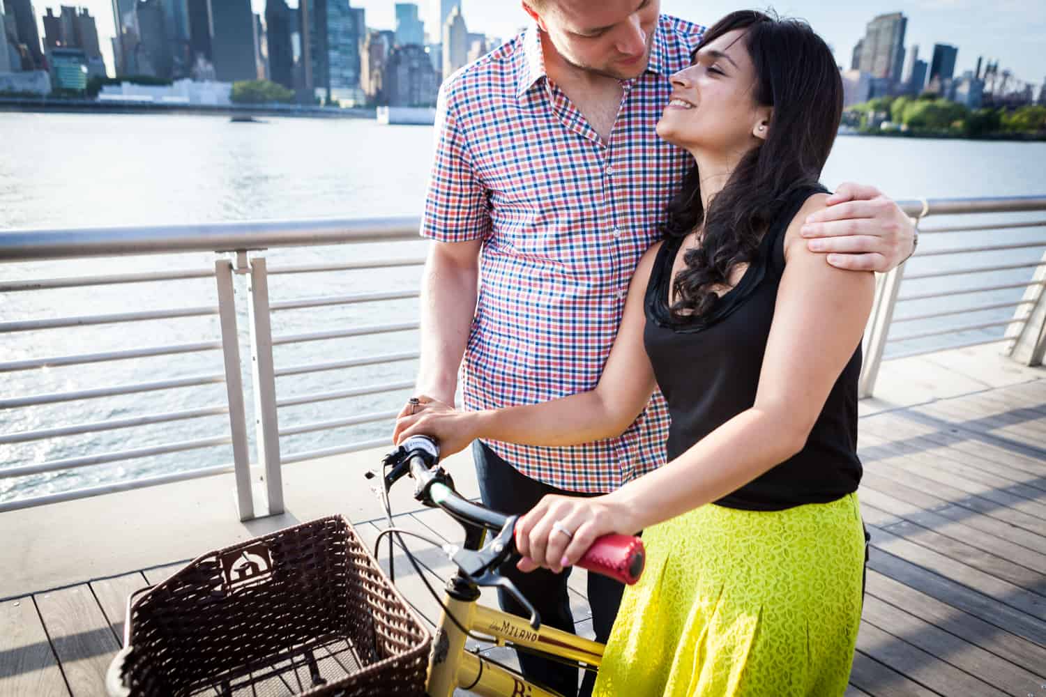 Man with woman on bicycle on boardwalk at a Gantry Plaza State Park engagement shoot