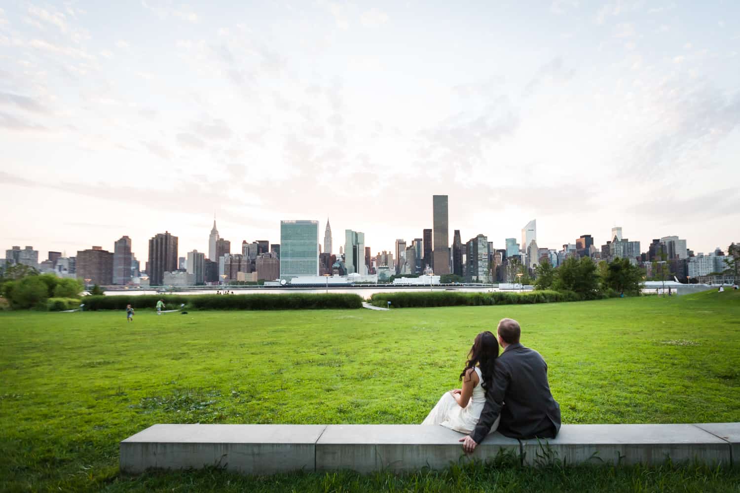 Couple sitting on stone wall watching NYC skyline at sunset