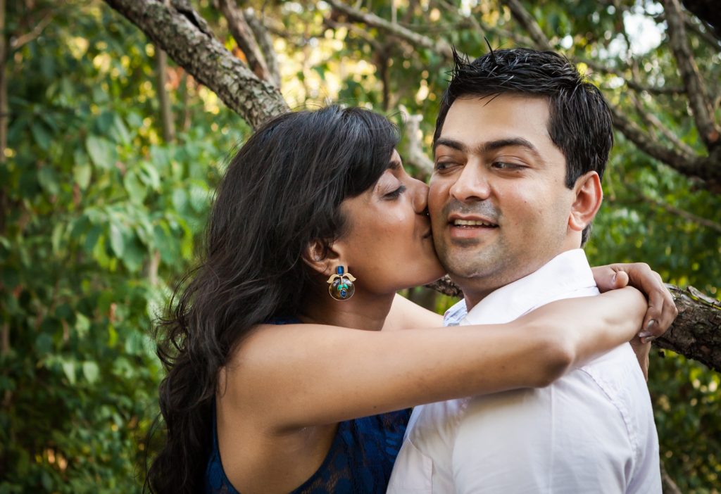 Woman kissing man on cheek in forest during a Central Park engagement shoot