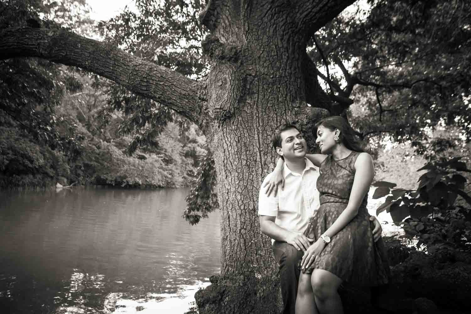 Black and white photo of woman sitting in man's lap by tree