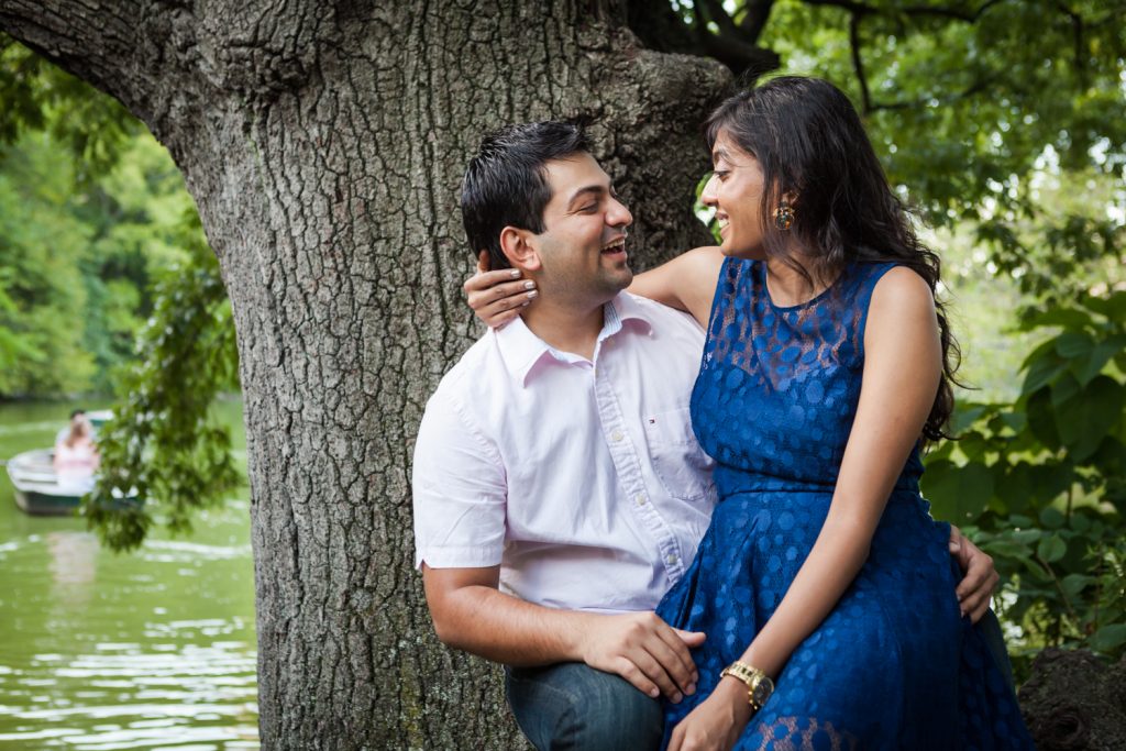 Woman sitting in man's lap by tree during a Central Park engagement shoot