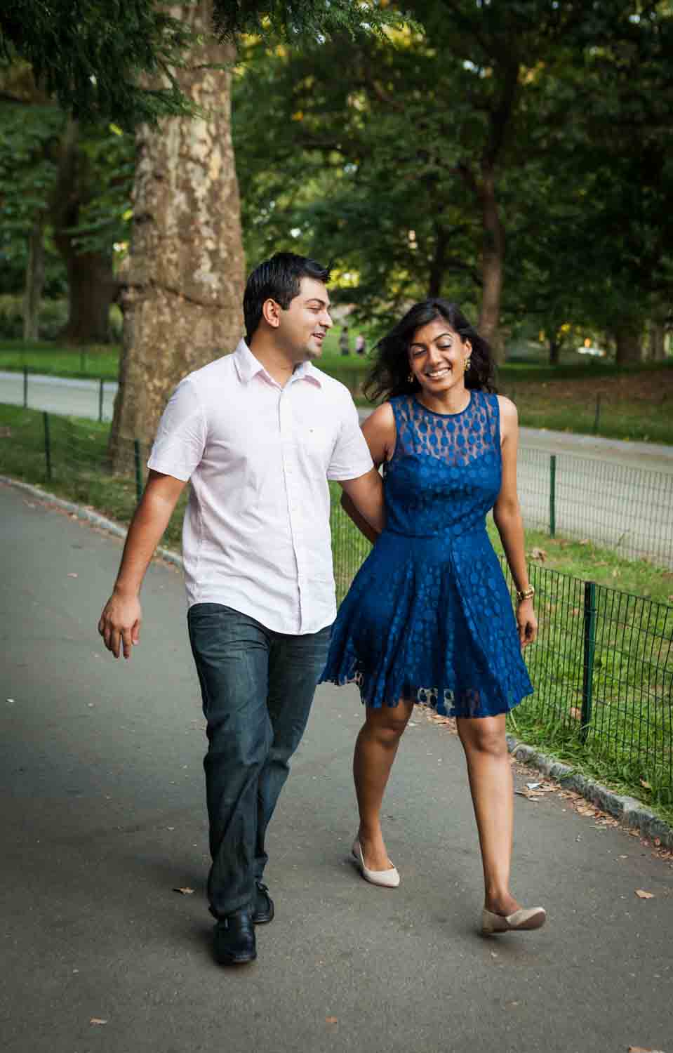 Couple walking along pathway Woman sitting in man's lap by tree during a Central Park engagement shoot