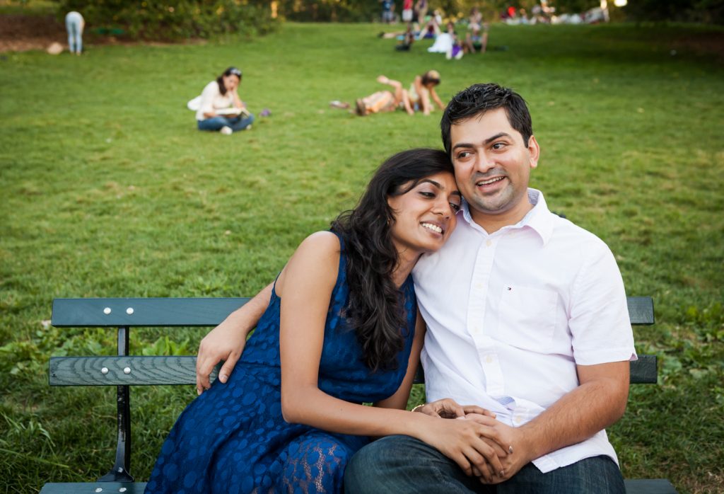 Couple sitting on bench Woman sitting in man's lap by tree during a Central Park engagement shoot